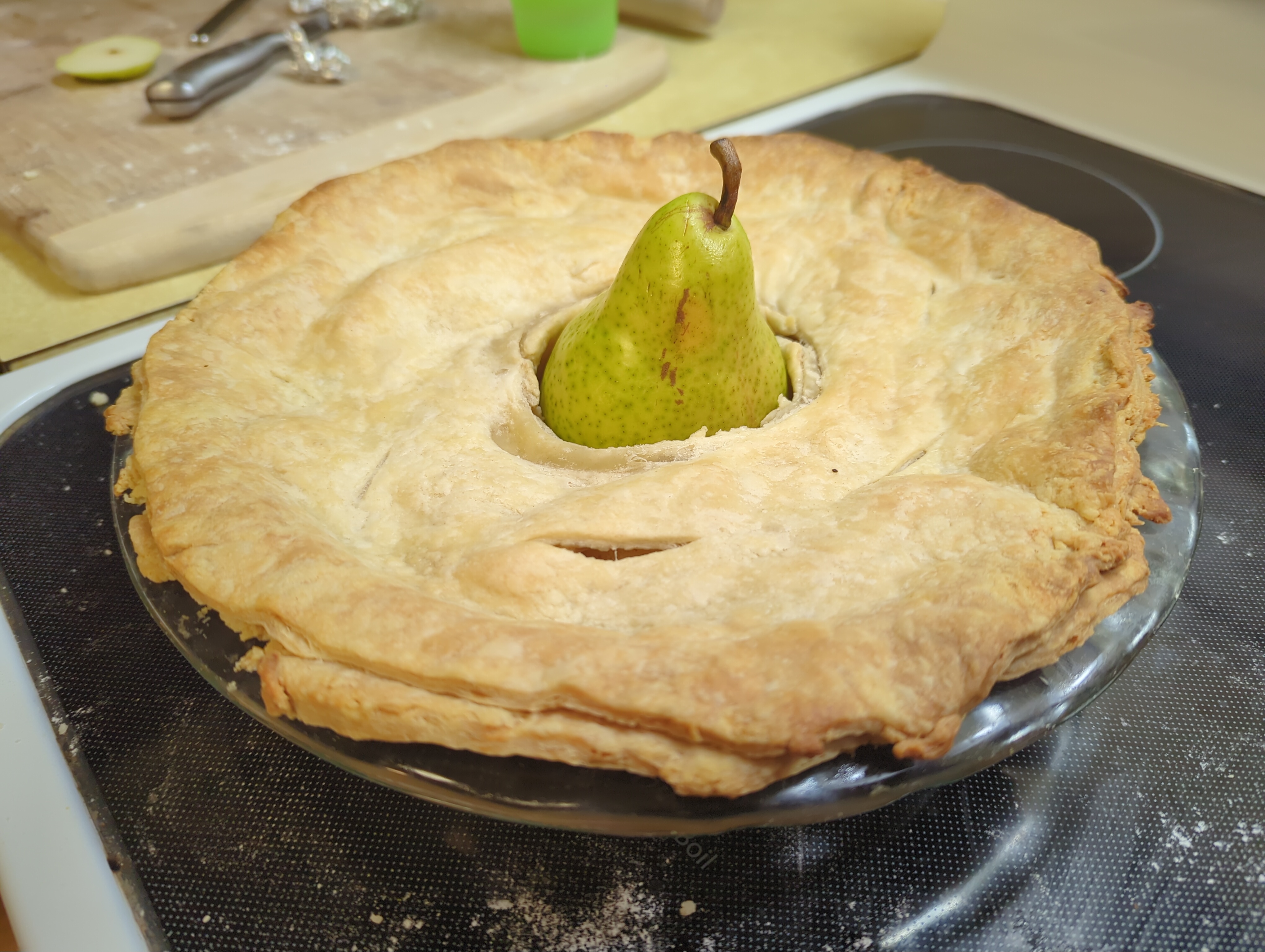 A pear pie with a pear sitting in the center, surrounded by the pie.